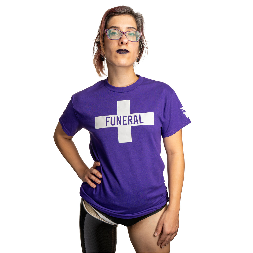 A model wearing a purple cotton unisex t-shirt featuring a funeral flag design in white. The funeral flag design is what you would see waving on a hearse at a funeral procession, it features a cross with "FUNERAL" on the horizontal part of the cross.