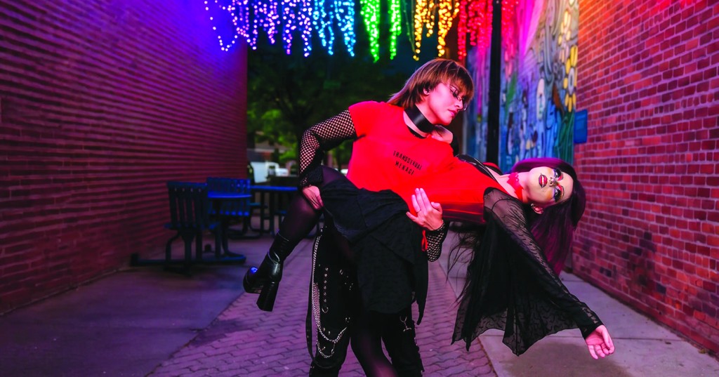 Two people in alternative clothing beneath rainbow lights